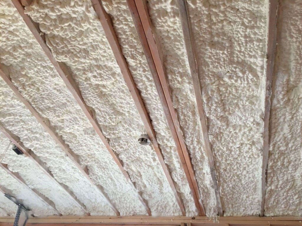 Spray foam insulation applied between wooden beams on a ceiling.