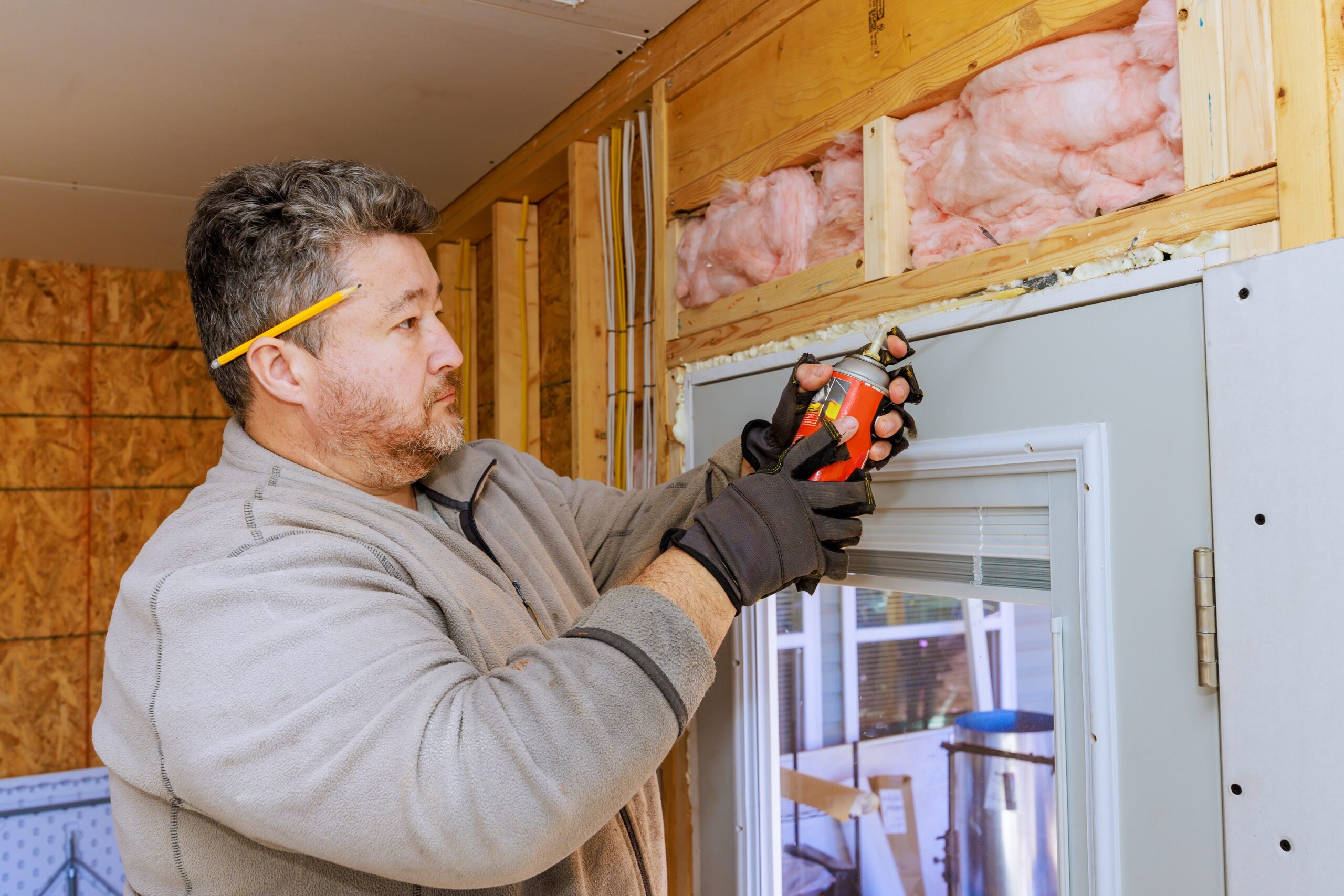 Man installing insulation above a window frame inside a house.