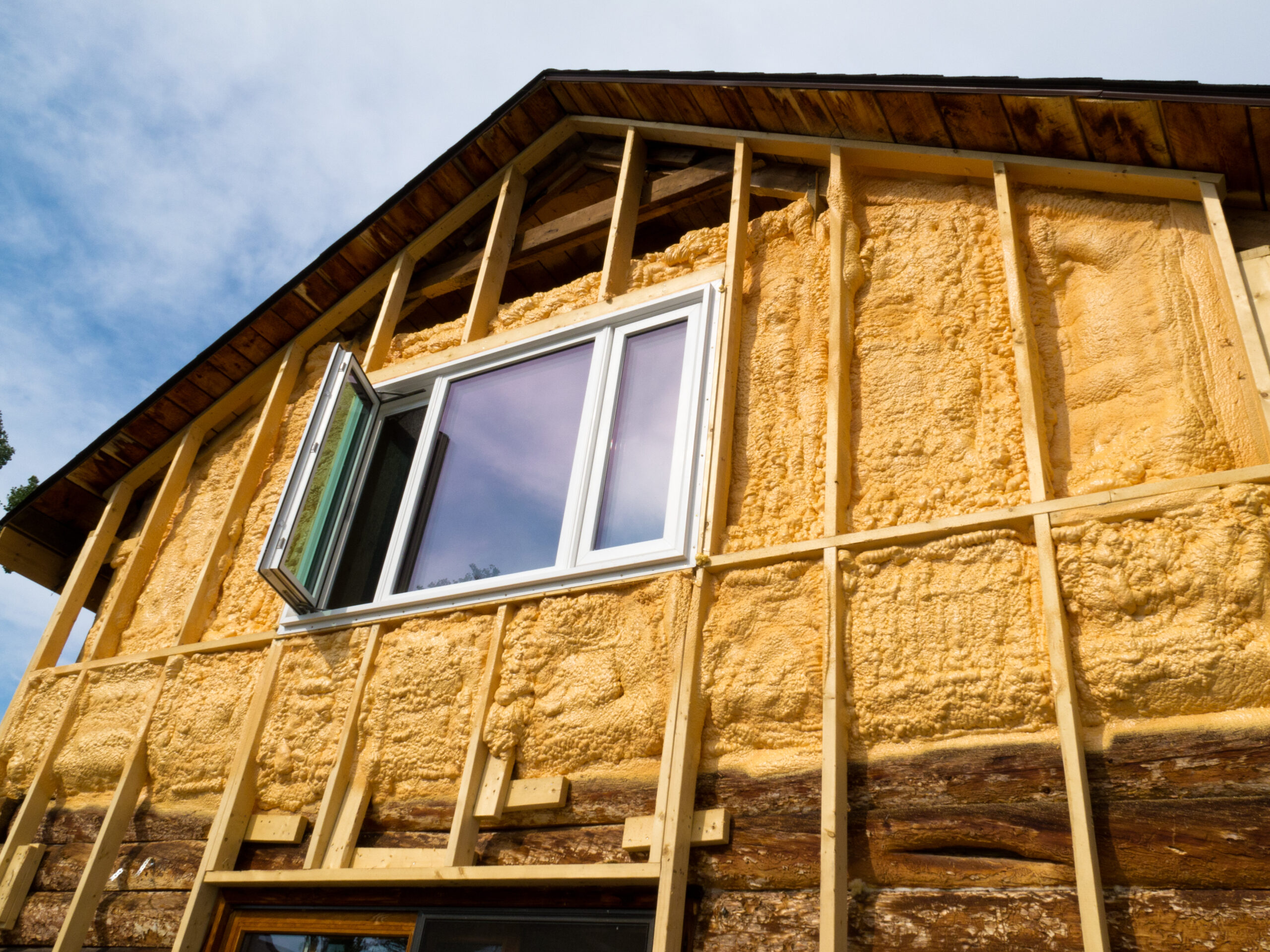 Exterior wall of a house insulated with spray foam, showing wooden framing.